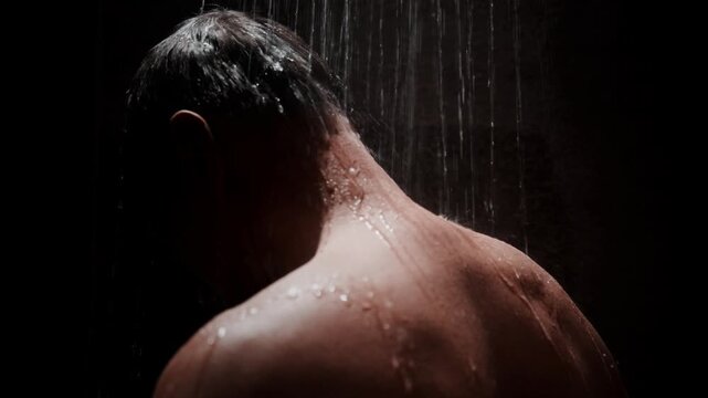 Dripping water falls on a man's back. Darkness surrounds the shower scene. He stands bare, shoulders tense, head bowed. Emotionless, he washes away tension or discomfort. Ideal for mood-driven