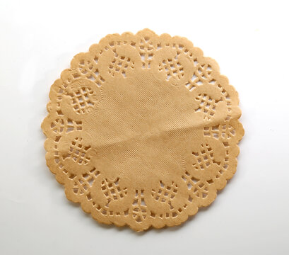 Round beige paper doily featuring intricate lace cutouts and a scalloped edge on white background.