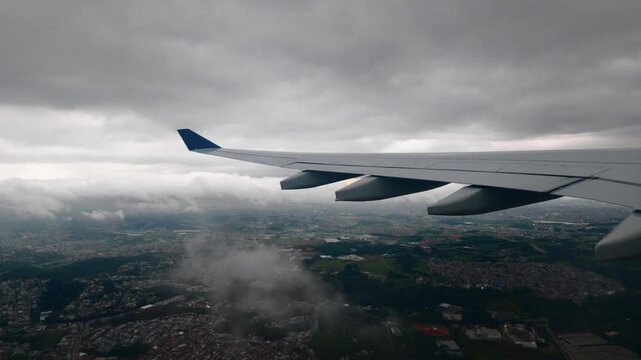 Airliner wing over a dense urban sprawl and a highway interchange under a grey overcast sky during the final approach to Guarulhos airport in Sao Paulo Brazil