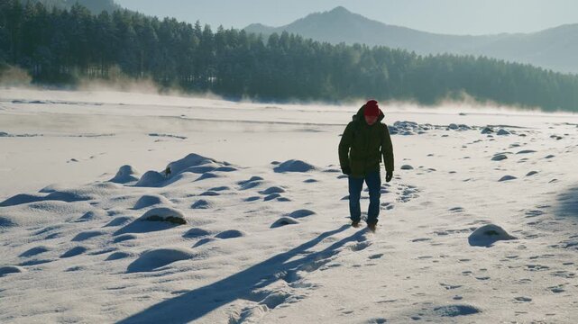 Lone figure walks across a vast, snowy expanse. Footprints mark the path behind them, leading deeper into the cold. Mist rises from the frozen ground, adding mystery to the scene