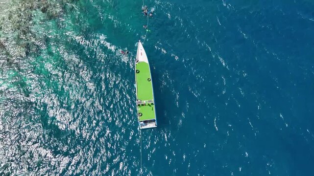 Aerial view of a white boat with people swimming in the deep blue sea of Karimunjawa, Central Java, Indonesia.