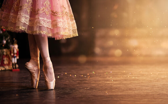 Ballerina en pointe wearing a pink tutu on stage with magical golden dust and a nutcracker