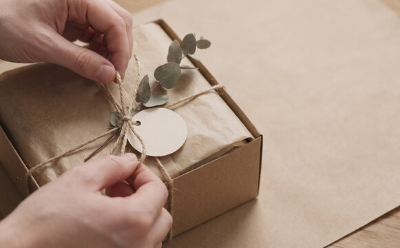Person wrapping handmade gift box with brown paper, twine, and eucalyptus sprig for special occasion