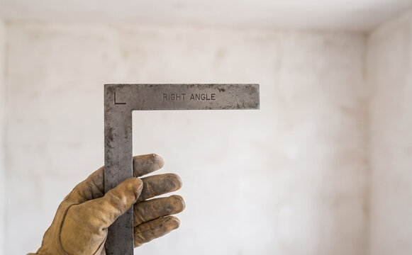 Worker holding a metal right angle square tool in a room under construction for precision measurement