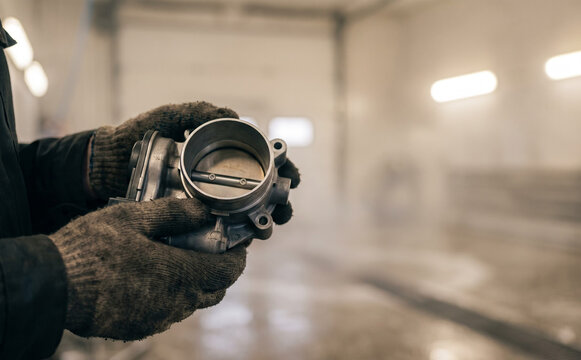 Mechanic holding car throttle body part in automotive repair shop for engine maintenance service