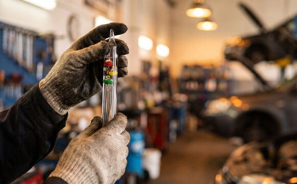 Mechanic holding coolant tester hydrometer in auto repair shop for car maintenance and testing