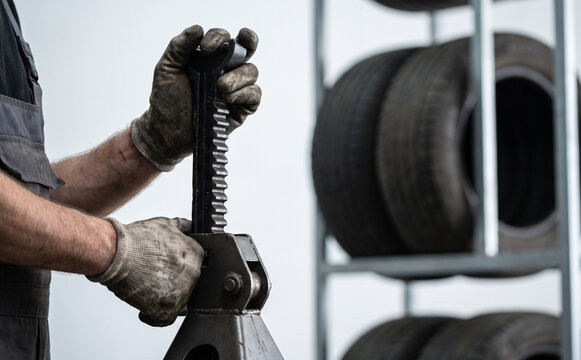Mechanic adjusting a ratchet jack stand in an auto repair shop with tires on racks