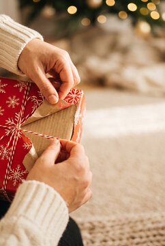 Woman wrapping a Christmas present with red snowflake paper and festive string in cozy interior