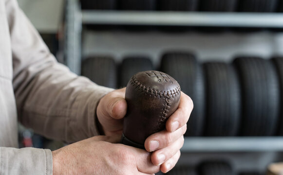 Mechanic holding a vintage leather gear shift knob in an auto repair shop with tires in the background