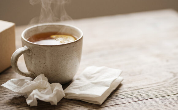 Hot lemon tea in a mug with tissues on a wooden table representing cold and flu recovery