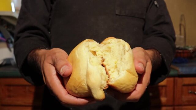 Baker breaking fresh homemade soft bread loaf in half in a professional kitchen, revealing the fluffy crumb texture of the delicious pastry in a close-up shot