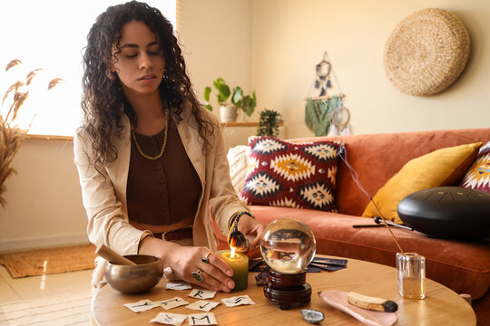 Spirituality and mindfulness practice, woman lighting candle with crystal ball and runes for divination and meditation in a cozy home living room