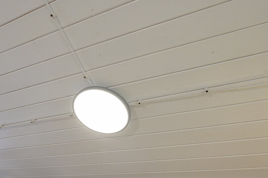 Round LED ceiling light mounted on white paneled ceiling, visible wiring, minimalist interior detail.
