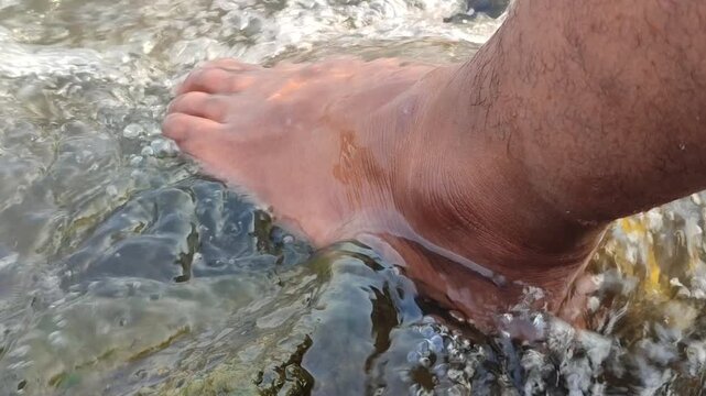 Bare feet rest in clear, flowing river water as gentle currents swirl around the ankles. A peaceful outdoor moment to relax, soothe tired muscles after a long walk, and enjoy the calming sounds of nat