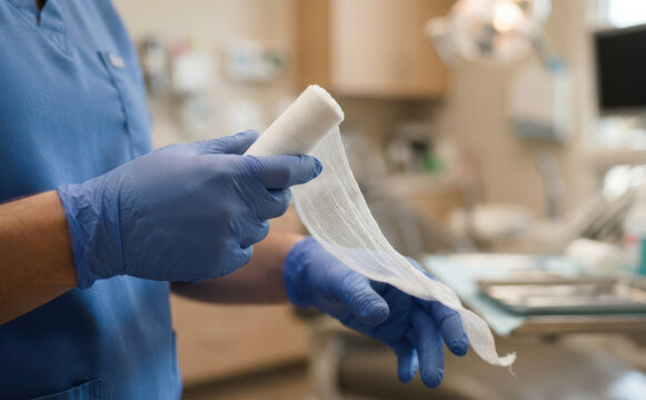 Medical professional in blue scrubs holding sterile bandage gauze in clinic, healthcare concept