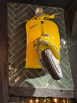 A yellow Vespa scooter front section mounted on a dark green tiled wall framed by wooden beams - Rouen, France - September 6, 2026