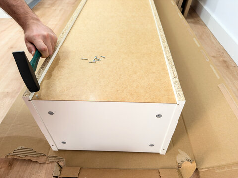 Long hardboard back panel with loose nails and a hammer at the edge