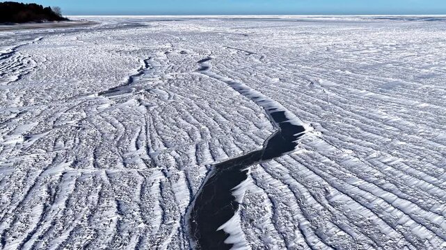 Aerial view of the frozen surface of Engure Lake with intricate ice patterns and a dark open water channel in Engure, Tukums Municipality, Latvia.
