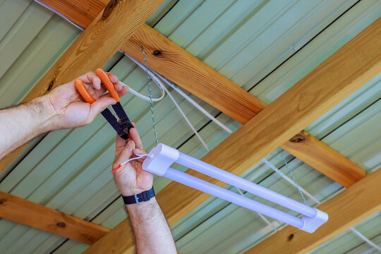 Person wiring suspended fluorescent light fixture beneath timber roof structure