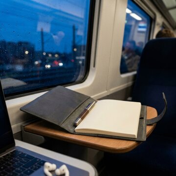 Open notebook and pen on a train tray table during evening commute.