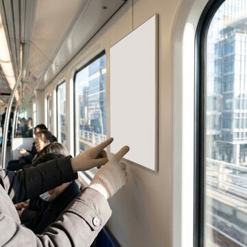 A person pointing at an empty blank advertisement poster inside a subway train carriage.