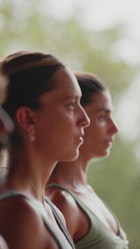Profiles of two women sitting with hands in prayer during meditation at the end of a yoga class, then raising their arms together, open-air studio in Puerto Escondido, Mexico.