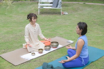 Two Asian women practicing meditation with singing bowls on gras © Sirirat Makprasert