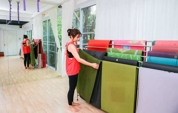 woman preparing colorful yoga mats inside a bright yoga studio with natural daylight and mirrors.