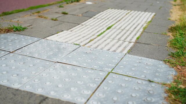 Close-up of tactile warning tiles and ribbed guidance paving on an accessible sidewalk in the Netherlands, designed to assist pedestrian navigation at a curb ramp.
