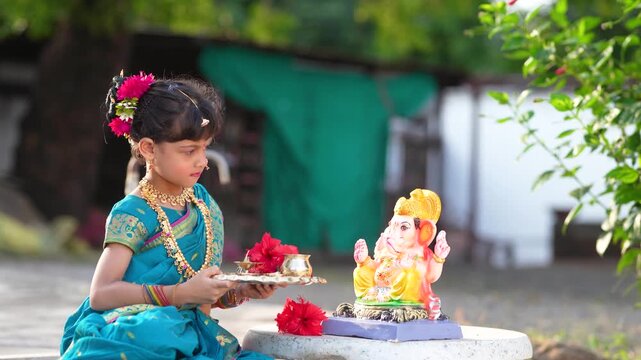 indian little girl doing puja of lord Ganesha sculpture at out of home