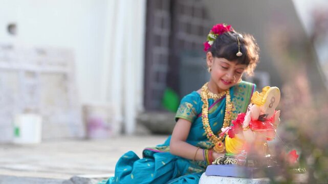 indian little girl doing puja of lord Ganesha sculpture at out of home