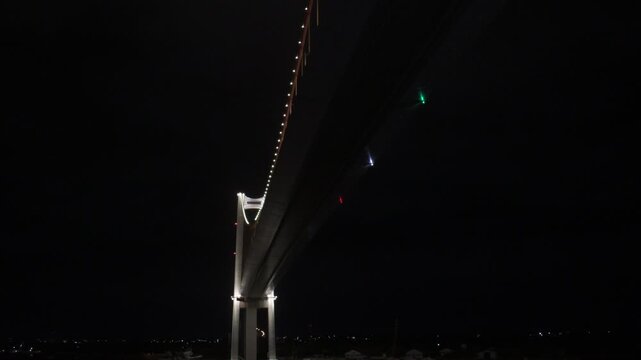 upward low angle view of the illuminated deck, cables, and navigation lights of the maputo katembe suspension bridge crossing maputo bay against a dark night sky