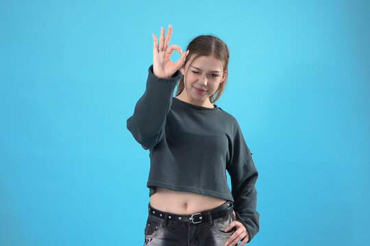 Young Girl Showing OK Gesture and Winking against Blue Background