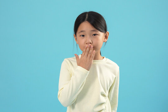 Surprised Young Asian Girl Covering Mouth on Blue Background