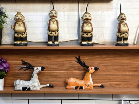 Traditional Indonesian wooden figurines and painted deer sculptures on wooden shelf, handcrafted Javanese folk art decoration with artificial flowers, cultural home decor
