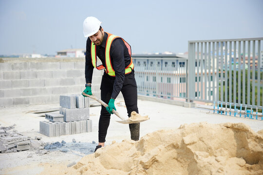 Construction worker is shoveling sand on a sunny day. He is in the process of building something new.