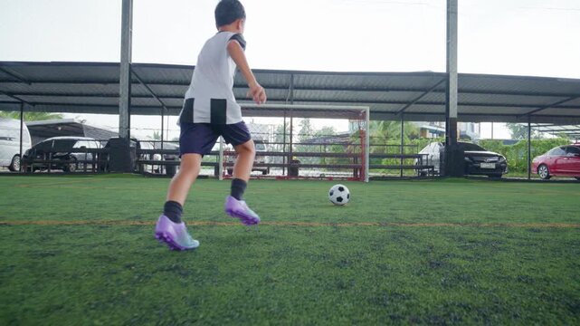Close-up of a boy kicking a soccer ball on a green turf field, with sharp detail and frozen motion, representing youth sports, training, fitness and a healthy active lifestyle.