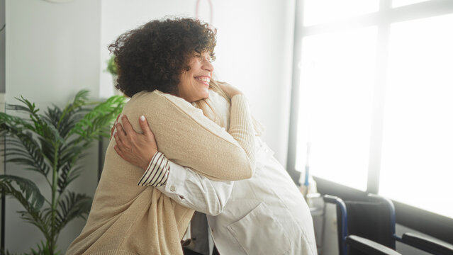 Middle age woman patient hugs doctor with stethoscope, arms wrapped around shoulders in clinic; comfort empathy support.