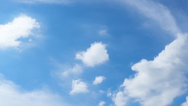 A captivating blue sky timelapse shows fragmented cumulus clouds stretching into irregular white formations, their soft edges dispersing as shifting winds reshape the sunlit summer atmosphere.

