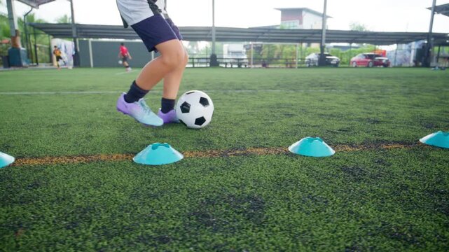 Close-up of a boy kicking a soccer ball on a green turf field, with sharp detail and frozen motion, representing youth sports, training, fitness and a healthy active lifestyle.