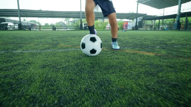 Close-up of a boy kicking a soccer ball on a green turf field, with sharp detail and frozen motion, representing youth sports, training, fitness and a healthy active lifestyle.