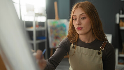 Woman painter holding brush and touching chin with hand while applying a stroke to canvas in studio  contemplation. © Krakenimages.com