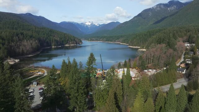 Capilano Lake Valley By Lush Evergreen Forest And Snowcapped Mountain Peaks In North Vancouver, British Columbia, Canada. - aerial ascend shot