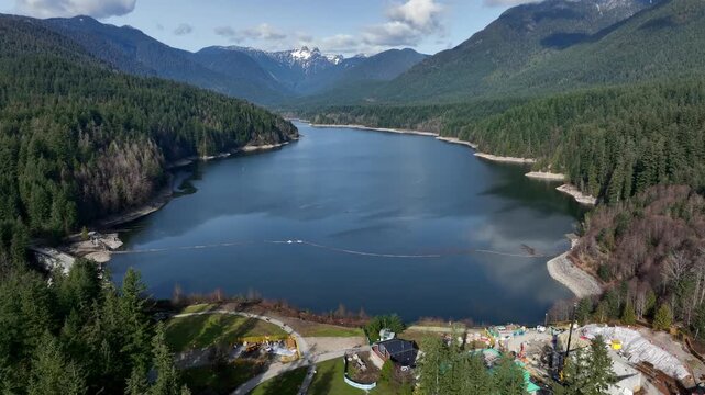 Capilano Reservoir With Calm Between Deep Green Woodland Hills And Mountain Slopes In North Vancouver, British Columbia, Canada. - aerial pullback shot