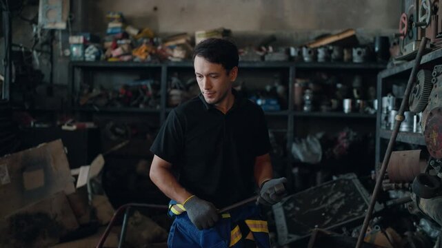 Young man works in cluttered workshop. He wears gloves and focused expression. Surrounding shelves hold tools and parts