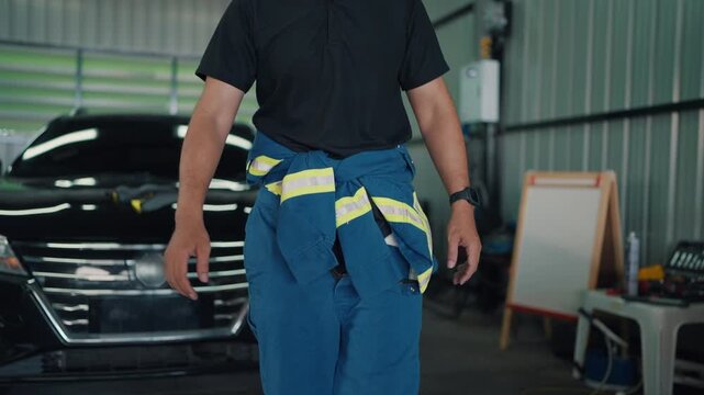 Mechanic stands confidently beside a car. His arms cross, face shows friendly assurance. Workshop background includes tools and a whiteboard
