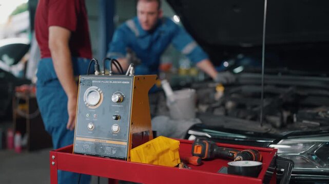 Two mechanics work under car's open hood. One leans over engine, adjusting parts with care. The other stands nearby, observing closely