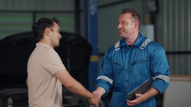 Mechanic shows customer a tablet with repair details. Customer looks curious, listens attentively. Vehicle is open, engine exposed in garage