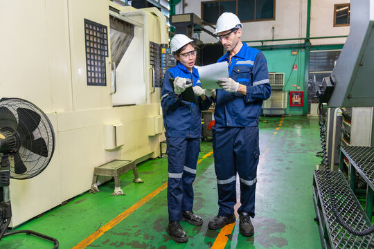 Industrial engineers discussing paperwork and tablet in CNC factory, Technicians in safety helmets reviewing machine maintenance documents near CNC equipment