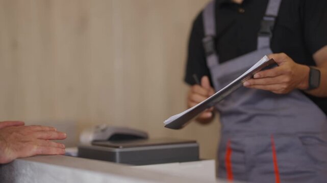 Man points to documents during service interaction. Worker holds tablet, preparing for transaction. Transaction occurs at counter. Ideal for business